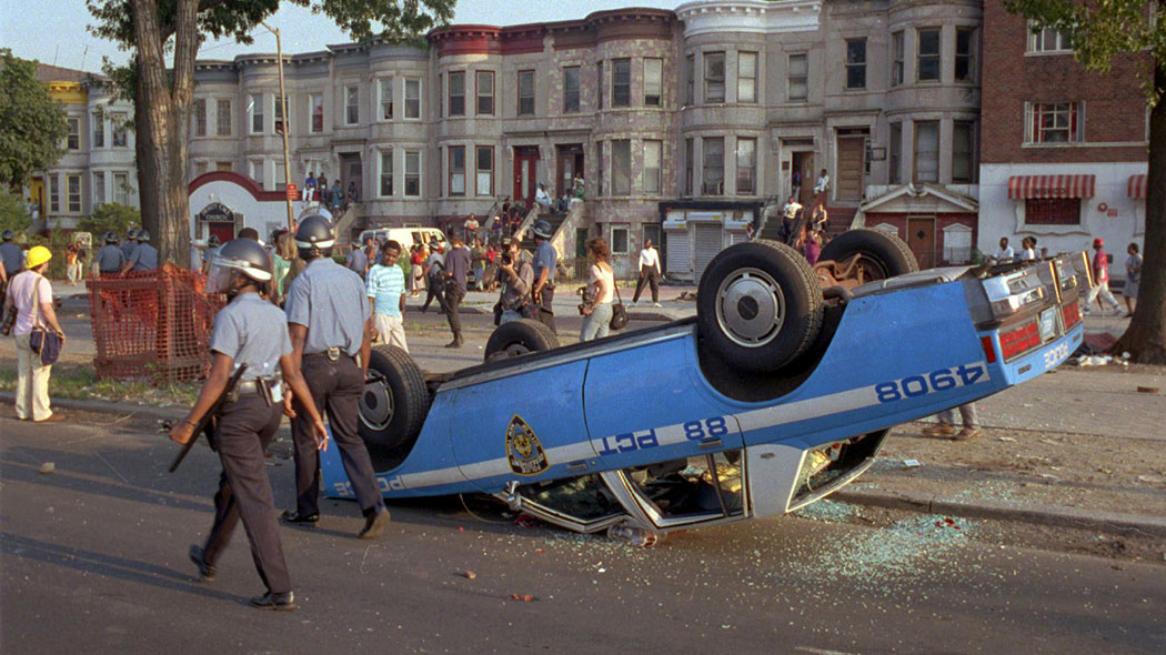 Police in riot gear walk past a police car that was overturned by rioters in the Crown Heights section of the Brooklyn borough of New York, where racial violence flared for days.