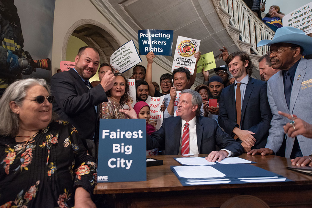New York City Mayor Bill de Blasio signs legislation last year to cap for-hire vehicles and mandate a minimum wage for drivers.