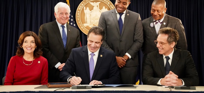 Gov. Andrew Cuomo signs voting reform legislation flanked by Lt. Gov. Kathy Hochul (left), Assemblyman Charles Lavine, state Senators Zellnor Myrie and James Sanders Jr., and Ben Stiller.